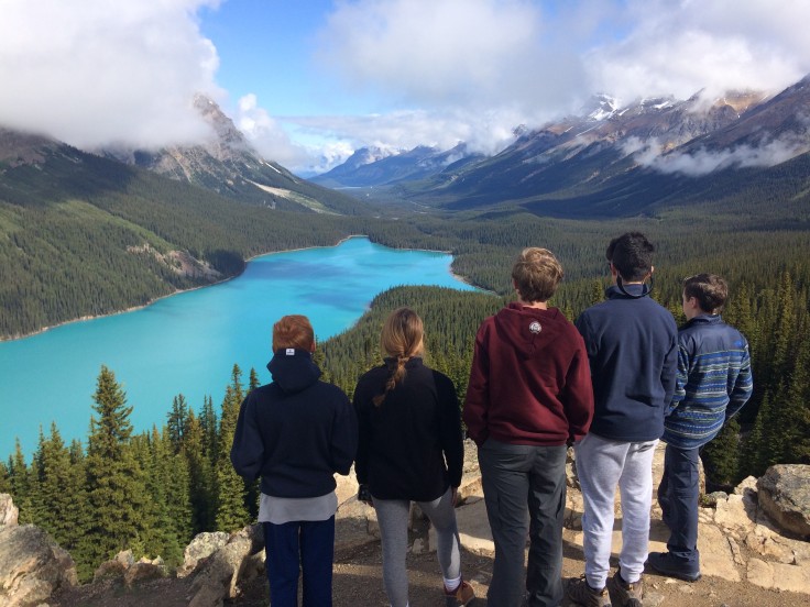 Young adults look out at a bright turqouise lake surrounded by snow-capped mountains in Canada